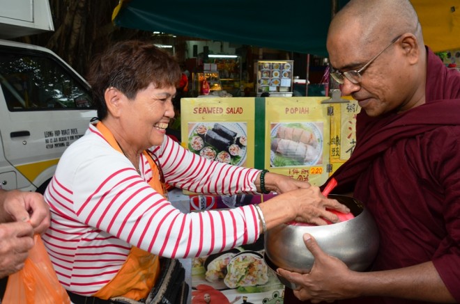 Stall owners and market-goers happily offering alms-food to the venerable monks.
