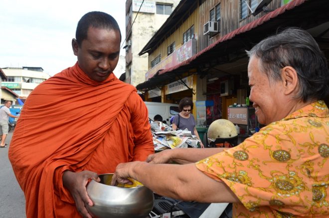 An elderly devotee offering alms with joy at the Seri Kembangan morning market. 